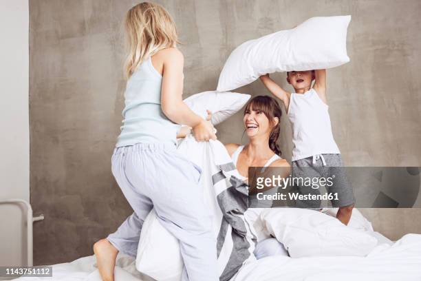 mother and children having fun, having a pillow fight in bed - luta de almofada imagens e fotografias de stock