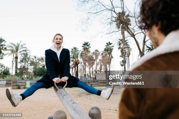 exuberant couple on a seesaw at a playground - seesaw foto e immagini stock