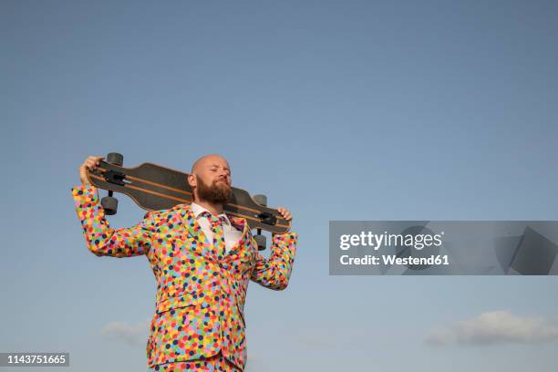 bearded man with longboard on his shoulders wearing suit with colourful polka-dots - colored clothes stock-fotos und bilder