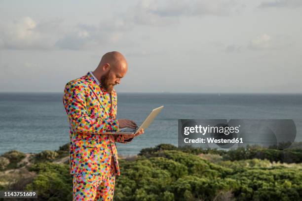 man wearing suit with colourful polka-dots using laptop outdoors - multi coloured suit stock pictures, royalty-free photos & images