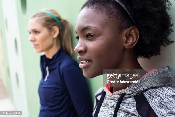 two sporty young women relaxing after running in the city - casual woman pensive side view stockfoto's en -beelden
