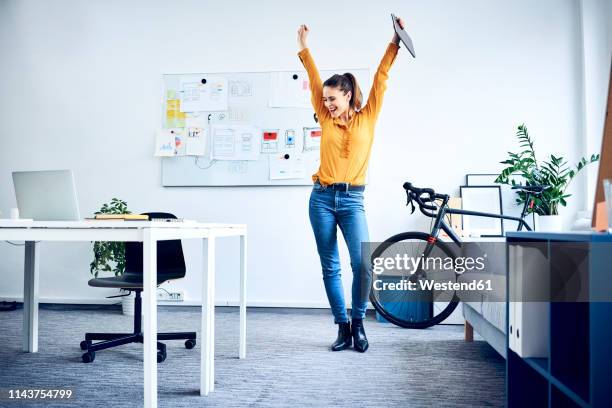 happy young businesswoman cheering in office - arms raised stock-fotos und bilder