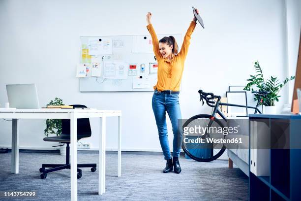 happy young businesswoman cheering in office - braccia alzate foto e immagini stock