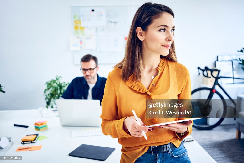 Businesswoman holding tablet in office with colleague in background