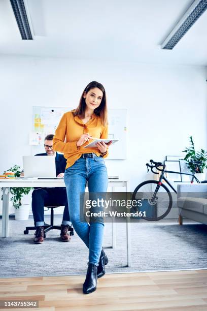 portrait of businesswoman using tablet in office with colleague in background - graphics tablet stock pictures, royalty-free photos & images