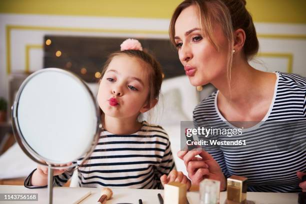 mother and daughter applying make up together, using lipstick - matching outfits stock-fotos und bilder