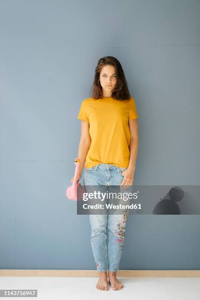 woman leaning on wall, holding flamingo shaped watering can - tshirt jeans stockfoto's en -beelden