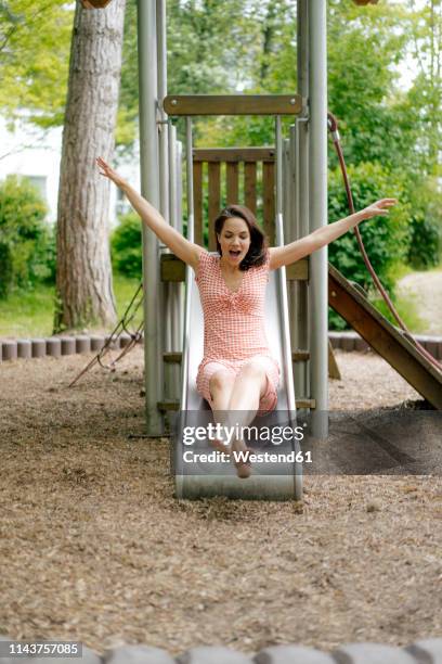 woman sliding on a slide on a playground - rutsche stock-fotos und bilder