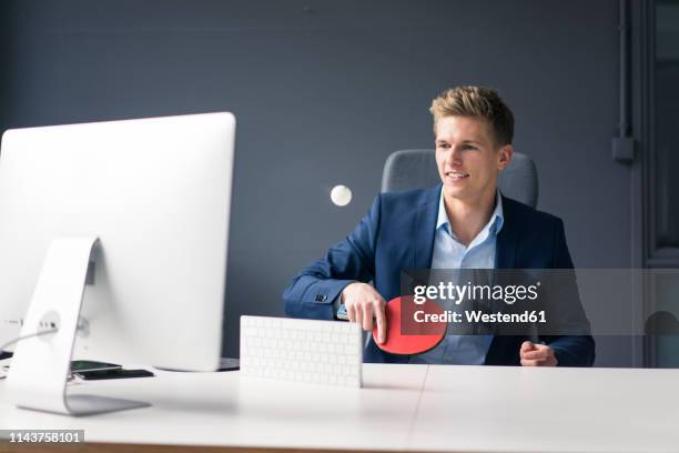 young businessman sitting at desk in office playing table tennis - men's table tennis stock pictures, royalty-free photos & images
