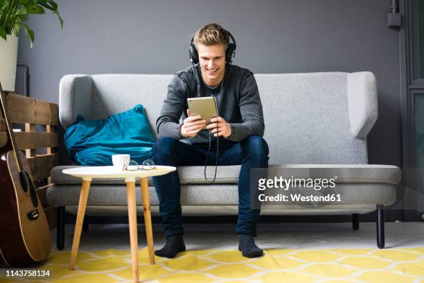 smiling young man with guitar, tablet and headphones sitting on couch - watching youtube stock pictures, royalty-free photos & images