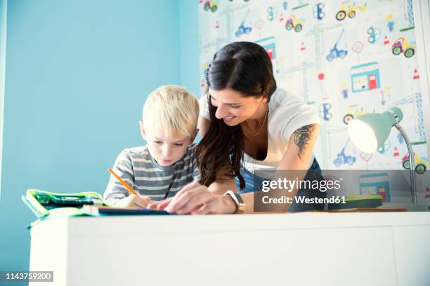 mother helping son doing homework at desk - estudiando flexo fotografías e imágenes de stock