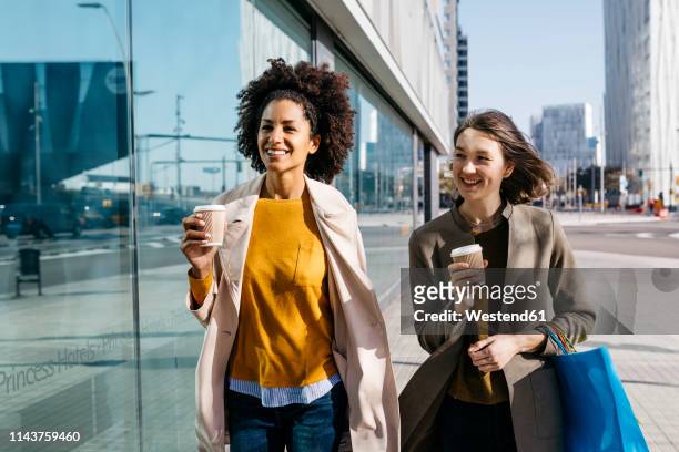 two happy women with shopping bags and takeaway coffee walking in the city - shopping center stock-fotos und bilder