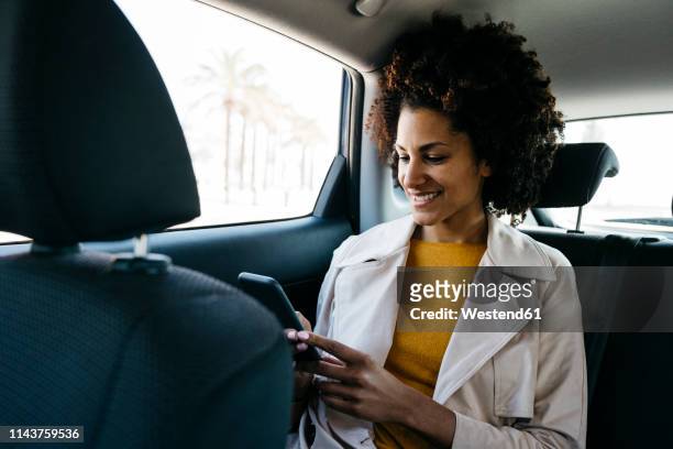 smiling woman sitting in back seat of a car using cell phone - taxi españa stockfoto's en -beelden