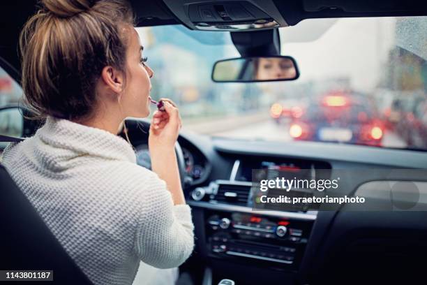 junges mädchen setzt lippenstift in den stau an regnerischen tag - abgelenkt stock-fotos und bilder