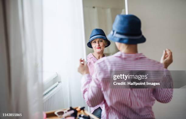 a rear view of active senior woman trying on a new hat, looking in the mirror. - passend stock-fotos und bilder