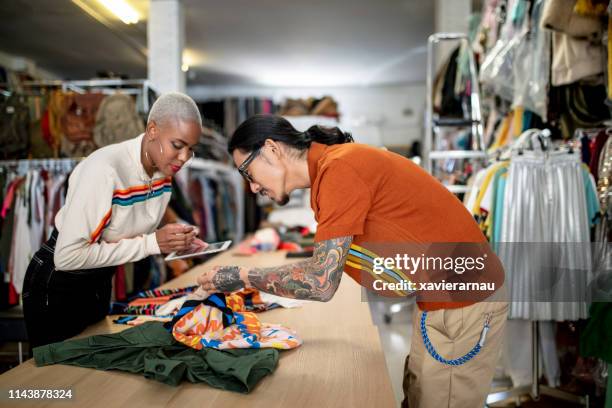 collègues utilisant la tablette pc tout en vérifiant textile - créateur de mode photos et images de collection