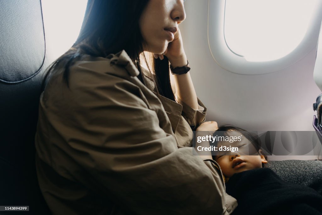 Little daughter sleeping on mother's lap while travelling on airplane