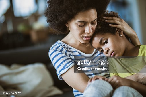 Young black mother taking care of her sad little daughter at home. Young black mother taking care of her sad little daughter at home.