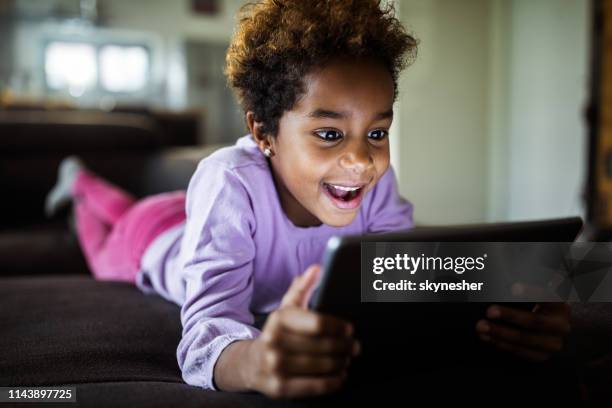 glückliches schwarzes mädchen genießen, während sie cartoons auf touchpad zu hause. - child animated watching stock-fotos und bilder