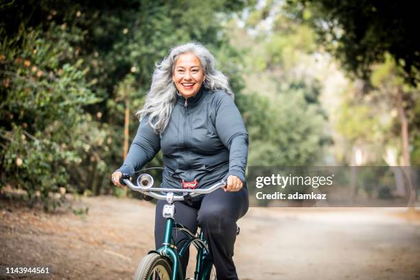 senior mexican frau reiten fahrrad - radrennfahrer stock-fotos und bilder