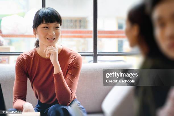 mujer joven empresaria asiática sonriendo y discutiendo ideas con colega - entrevista coletiva fotografías e imágenes de stock