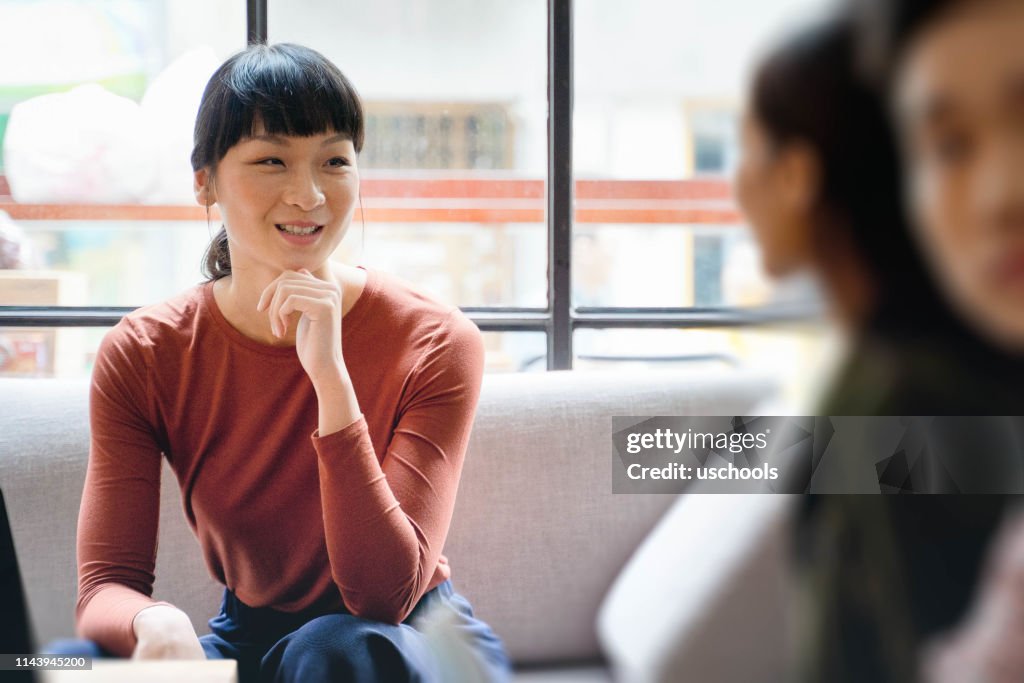 Giovane imprenditrice asiatica sorridente e discutendo idee con la collega