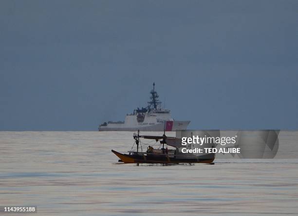 This photo taken on May 14 Filipino fishermen aboard their boat sails past US coastguard ship Bertholf during a joint exercise between Philippine and...