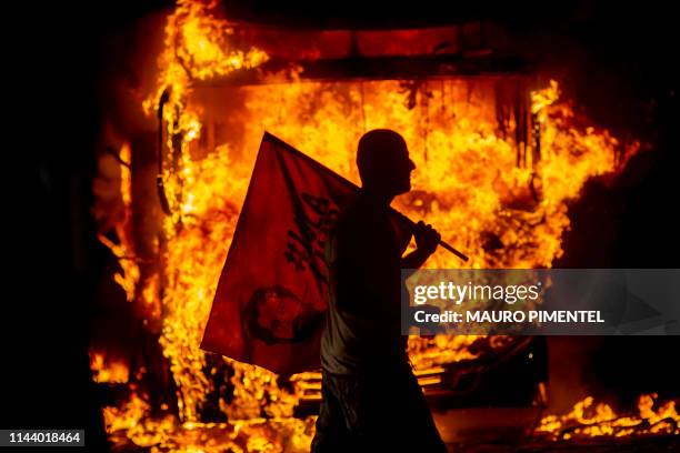 Man holds a flag depicting former Brazilian President Luis Inacio Lula da Silva past a bus in flames during a protest organized by the National...