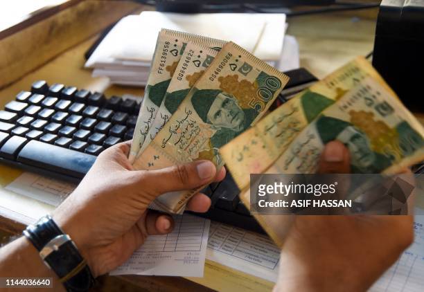 Pakistani man counts Pakistan's rupees at his shop in Karachi on May 16, 2019. Pakistan's rupee dropped to an all-time low of 146.5 to the dollar on...