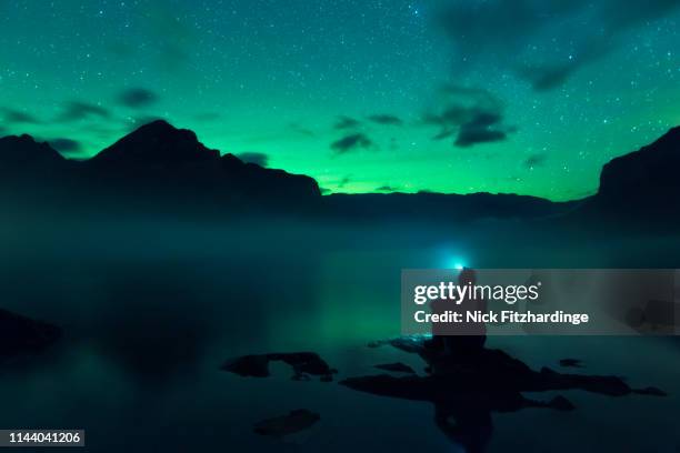 watching the aurora borealis glowing on the horizon from lake minnewanka, banff national park, alberta, canada - see lake minnewanka stock-fotos und bilder