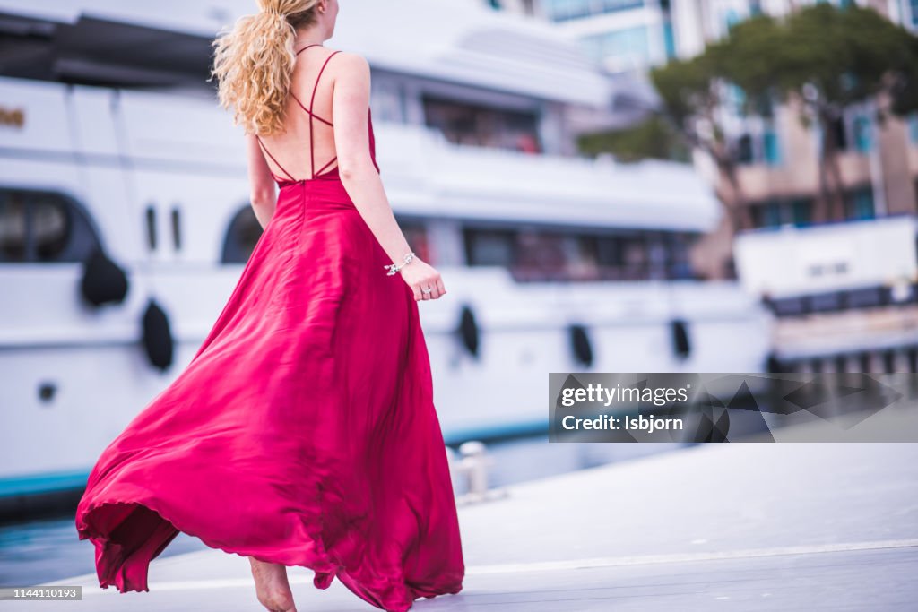 Senhora de Blondie no vestido de seda vermelho que funciona afastado.