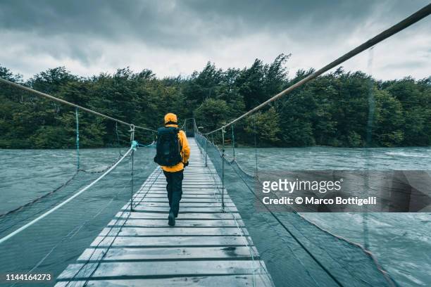 tourist walking on a wooden bridge over a swollen river - cruzar puente fotografías e imágenes de stock