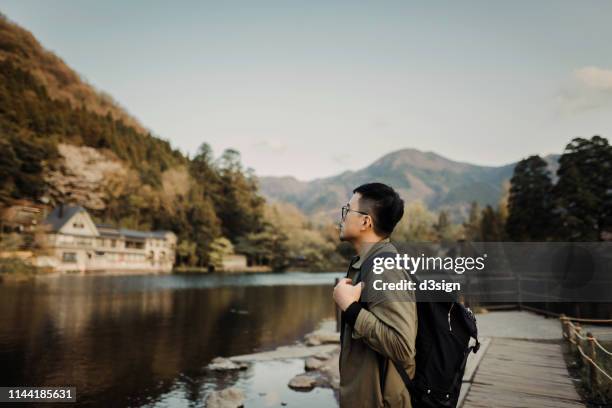 young asian man with backpack sightseeing at lake relaxing and enjoying the beautiful scenics - fukuoka city stock-fotos und bilder