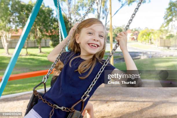 happy girl smiling while playing on swings at the park - swinging stock pictures, royalty-free photos & images