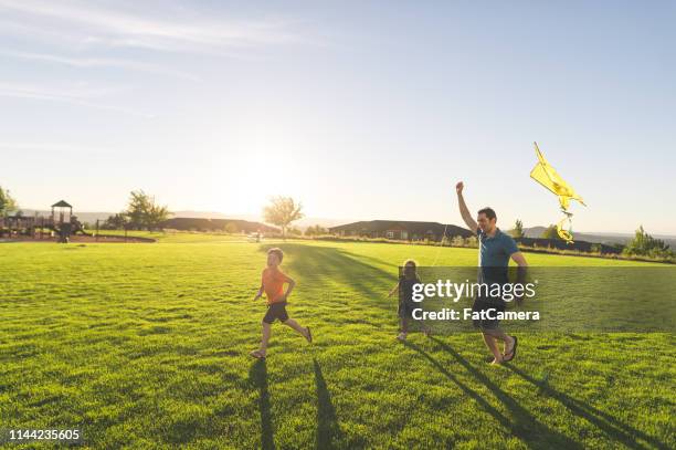 papa fliegende drachen mit seinen kindern im park - flying child stock-fotos und bilder