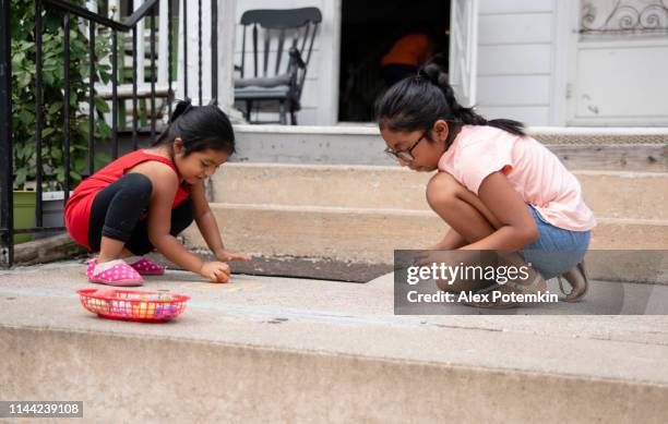 dos pequeñas chicas latinas mexicanas-americanas, hermanas, dibujando con tiza en el porche de su casa en pensilvania - hot mexican girls fotografías e imágenes de stock