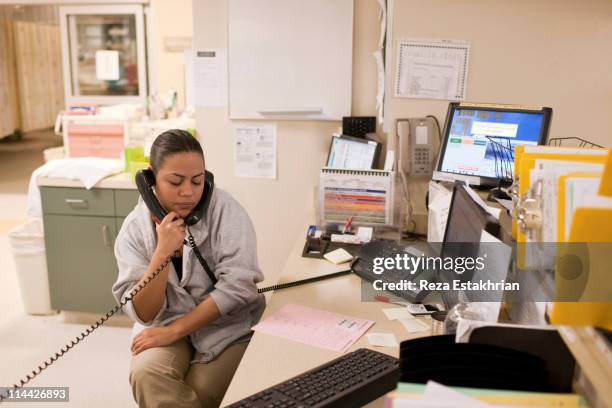 nurse holds two phones to her ears - schwesterntisch stock-fotos und bilder