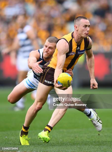 Tom Scully of the Hawks handballs whilst being tackled by Sam Menegola of the Cats during the round 5 AFL match between Hawthorn and Geelong at...