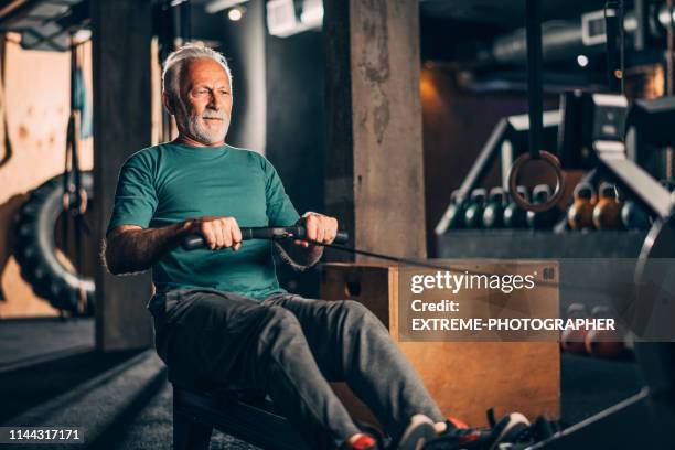 desportista idoso ativo que faz um exercício em uma máquina de enfileiramento em uma ginástica do crossfit - só um homem idoso - fotografias e filmes do acervo