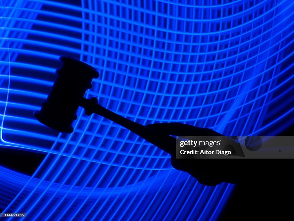 Hand holding a judge's hammer in a futuristic environment