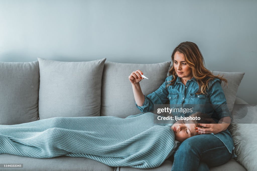 Mother reads thermometer while son laying sick in bed