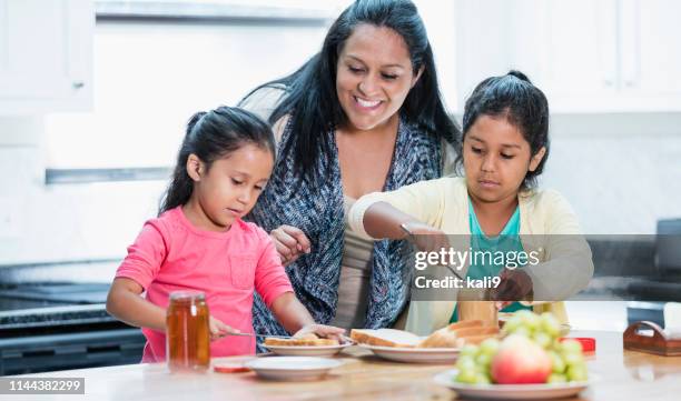 kleine spaanse meisjes maken pindakaas sandwiches - mother and child snacking stockfoto's en -beelden