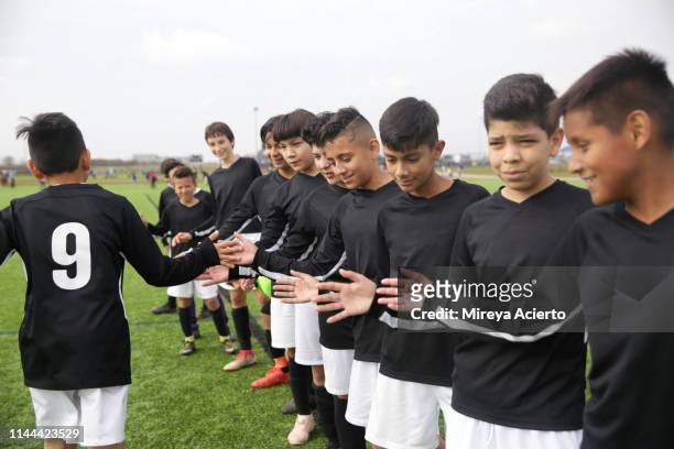 A group of teenage Latino soccer players congratulate their teammate on an outdoor soccer field.