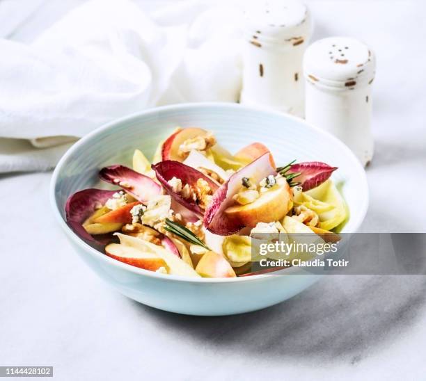 a bowl of endive salad with slices of apple, walnuts, and blue cheese on white background - chicoree stock-fotos und bilder