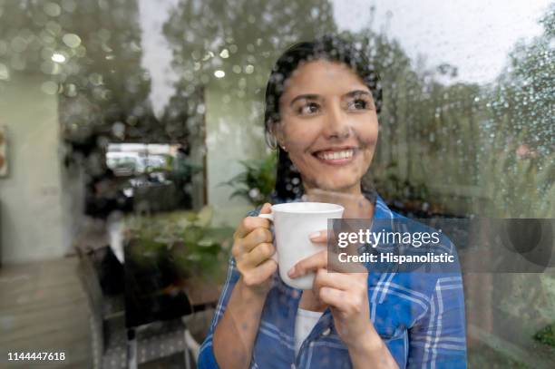 mooie vrouw thuis kijken door het raam op een regenachtige dag enjoyng een kopje koffie - women wearing see through clothing stockfoto's en -beelden