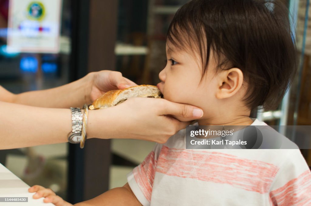 A baby boy is being fed by his mother with a sandwich