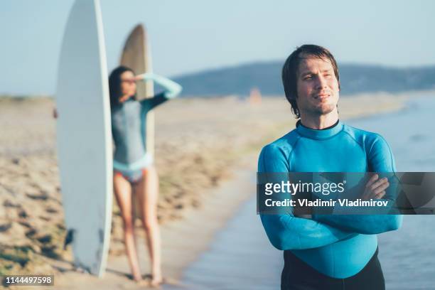 surfista maschio in piedi braccia incrociate sulla spiaggia - surfer wetsuit crossed foto e immagini stock