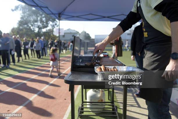 Man cooks sausages as voters stand in line outside a polling station during a federal election in Melbourne, Australia, on Saturday, May 18, 2019....