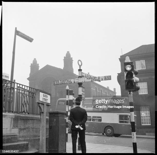 Swan Square, Burslem, Stoke-on-Trent, 1965-1968. A policeman standing beside a signpost at the junction of Queen Street and Swan Square with the...