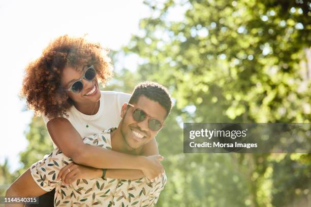 giovane coppia che si gode il giro in piggyback nella giornata di sole - mid twenties fun foto e immagini stock